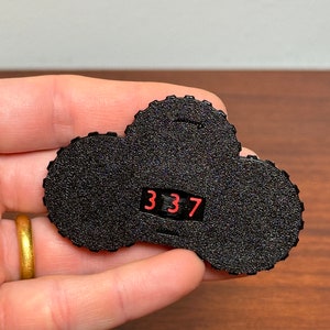 Puede incluir: Contador de plástico negro en forma de nube con una pantalla digital roja que muestra el número 337.