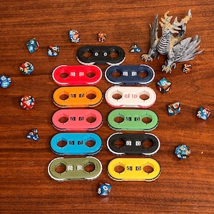 May include: A selection of multi-coloured dice and counters for tabletop games. The counters are in various colours, including black, red, orange, pink, blue, green, and yellow. A detailed dragon figurine is also present.
