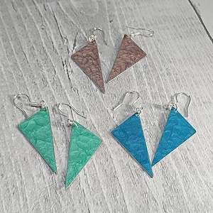 May include: A set of six triangle-shaped earrings with a textured surface. The earrings are available in three colours: brown, teal, and blue.