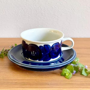 Könnte beinhalten: Ein weißes Keramik-Teetassen-Set mit passender Untertasse, das ein kräftiges, dunkelblaues Blumenmuster an der Außenseite der Tasse aufweist. Die Untertasse ist in einem einfarbigen Dunkelblau mit erhöhtem Rand gehalten und hat einen Henkel.