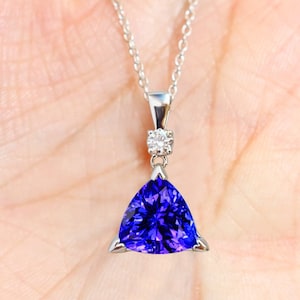 Könnte beinhalten: Eine silberne Kettenkette mit einem dreieckigen Anhänger, der mit einem großen violetten Edelstein und einem kleineren klaren Edelstein besetzt ist.
