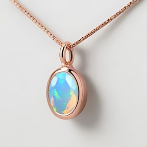 May include: A delicate rose gold necklace with a small oval opal pendant. The opal is iridescent with shades of blue, green, and white.