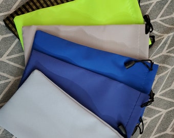 May include: Five different colored drawstring pouches for glasses or other small items. The pouches are made of a soft, smooth fabric and have a drawstring closure. The colors are black and gold striped, neon green, light gray, blue, and light blue.