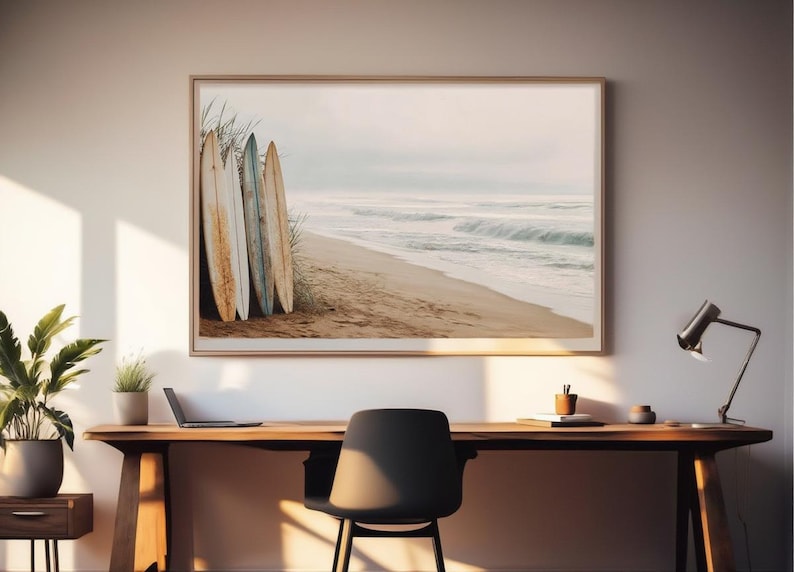 May include: A framed print featuring a beach scene with surfboards. The artwork depicts several weathered surfboards leaning against beach grass on a sandy shore. The ocean waves and sky are visible in the background, creating a coastal theme.