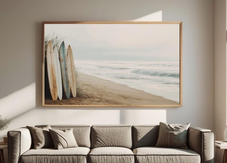 May include: A framed print featuring a beach scene with three surfboards leaning against dune grass. The surfboards are weathered with shades of brown, blue, and white. The ocean waves and sandy beach are visible in the background, creating a coastal theme.