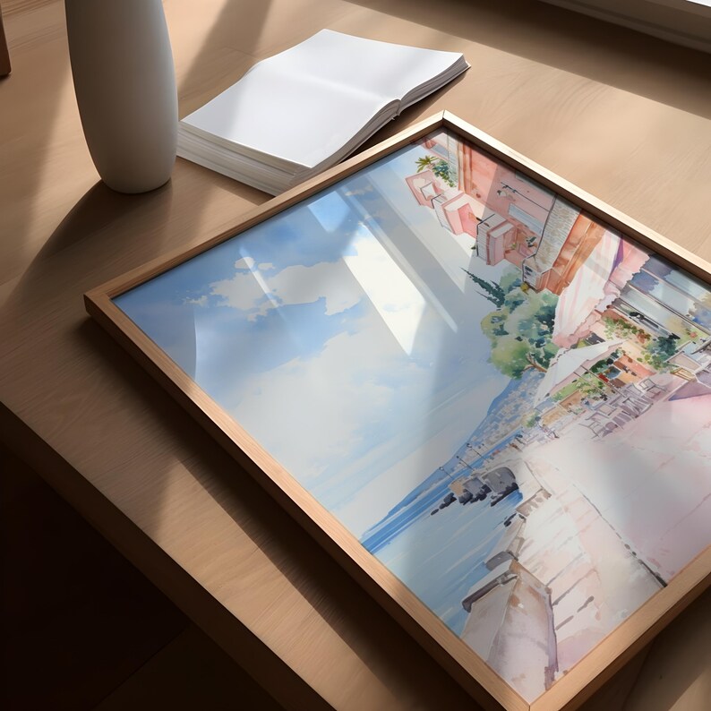 May include: A framed watercolor painting depicting a coastal town with buildings, a waterfront, and a blue sky with white clouds. The painting is in a light wood frame.