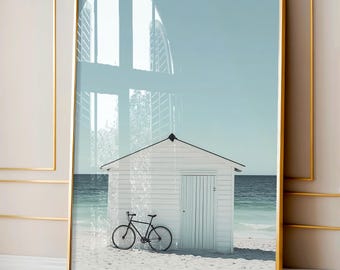 May include: A white beach house with a black bicycle in front of it. The house has a white door and white siding. The beach is sandy and the ocean is blue. The sky is light blue.