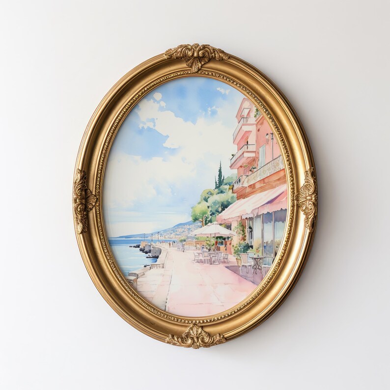 May include: A watercolor painting of a seaside town with a pink building, palm trees, and a cafe. The painting is framed in a gold oval frame.