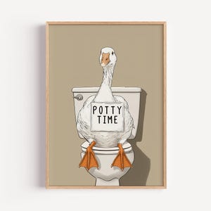 May include: A framed print features a white goose sitting on a toilet. The goose holds a sign that reads "POTTY TIME." The goose has orange feet and a beige background. The artwork is whimsical and humorous.