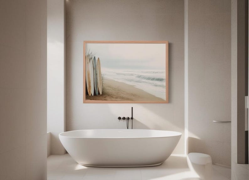 May include: A framed print of a beach scene with surfboards leaning against each other. The artwork is displayed above a white oval bathtub in a modern bathroom setting. The color palette is neutral with soft tones.