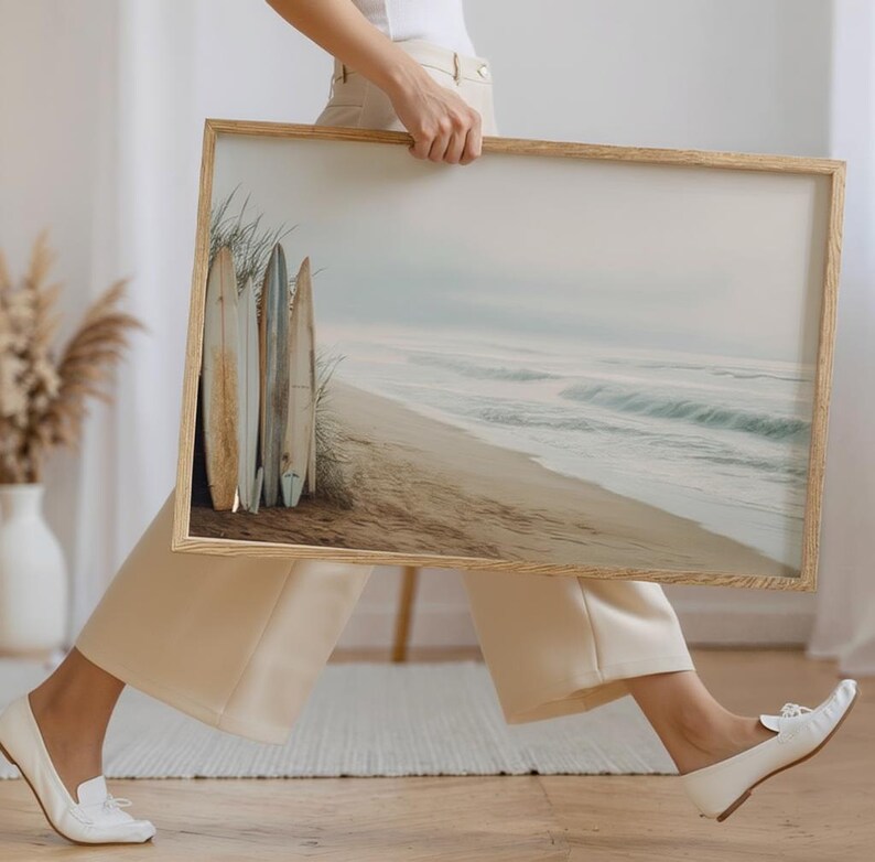 May include: A framed print featuring a serene beach scene with surfboards. The artwork depicts a sandy beach, ocean waves, and a cloudy sky. The surfboards are leaning against the dunes, adding a coastal theme to the artwork.