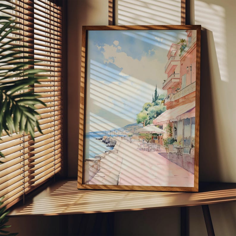 May include: A framed watercolor painting of a seaside town with buildings, palm trees, and a blue sky. The painting is in a wooden frame and is hanging on a wall.