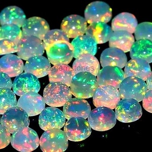 Könnte beinhalten: Eine Sammlung von irisierenden Opal-Cabochons in verschiedenen Schattierungen von Weiß, Grün und Rosa. Die Cabochons sind rund und haben eine glatte, polierte Oberfläche.