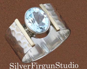 May include: A silver ring with a light blue oval gemstone and gold accents. The ring has a hammered texture on the silver band and the text "SilverFirgunStudio" is visible.