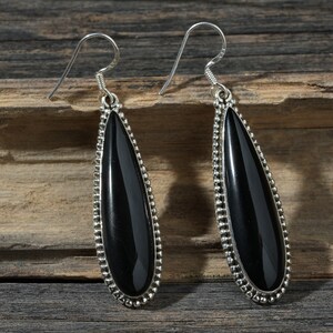 May include: A pair of silver dangle earrings with black teardrop-shaped stones. The stones are set in a beaded silver frame.