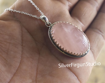 May include: A silver chain necklace with a pink oval rose quartz pendant. The pendant has a silver border with a scalloped edge.