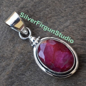 Peut inclure: Un pendentif en argent avec une grande pierre précieuse en rubis de forme ovale. Le rubis est de couleur rouge foncé et a une taille facetée. Le pendentif est serti dans une bélière en argent.