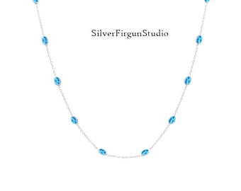 May include: A delicate silver chain necklace featuring evenly spaced, small oval-shaped bright blue stones. The text SilverFirgunStudio is centred in the upper portion of the image. The necklace is arranged in a gentle U-shaped curve against a white background.
