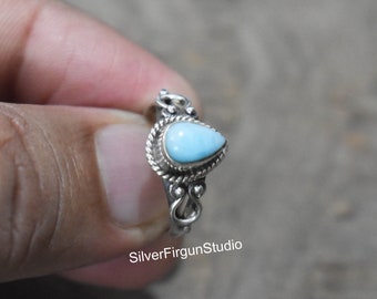 May include: A silver ring with a teardrop-shaped blue gemstone set in a delicate silver design. The ring is on a finger.