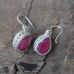 May include: A pair of silver earrings featuring teardrop-shaped ruby stones set in elaborate silver frames. The earrings have a delicate, ornate design.