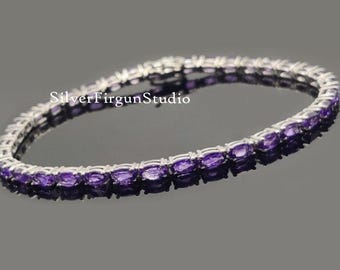 May include: A silver tennis bracelet with a row of purple amethyst stones.