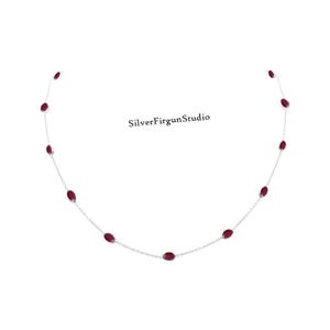 May include: A silver necklace with oval, deep red gemstones set along the chain. The necklace is shown against a white backdrop. The text "SilverFirgunStudio" is visible. A simple and elegant piece of jewellery.