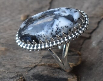 May include: A silver ring featuring a black and white dendritic agate stone set in a silver bezel with a decorative border.