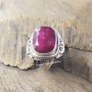 Peut inclure: Une bague en argent avec une grande pierre précieuse en rubis rouge foncé. La bague a un design complexe et orné.