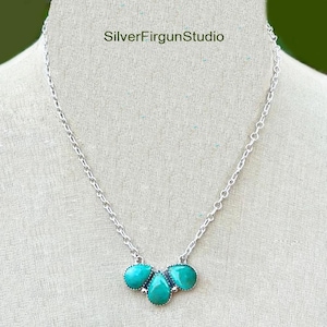 May include: A silver necklace with three turquoise gemstones in a teardrop shape. The stones are set in silver and linked by a silver chain. The text "SilverFirgunStudio" is visible at the top.