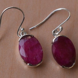May include: A pair of silver dangle earrings with oval-shaped ruby gemstones. The earrings have a simple design and are perfect for everyday wear.
