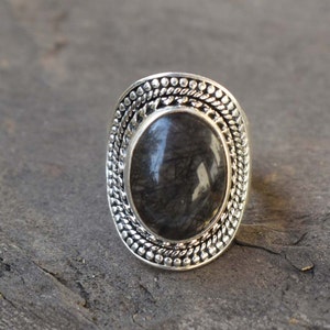 May include: A silver ring with a black oval gemstone set in a decorative silver bezel. The bezel has a textured design with small dots and lines.