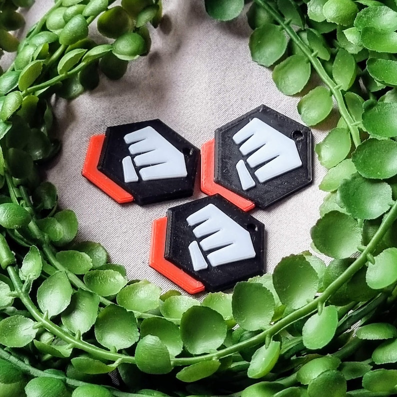 K&ouml;nnte beinhalten: Drei schwarze und wei&szlig;e sechseckige Schl&uuml;sselanh&auml;nger mit rotem Rand. Jeder Schl&uuml;sselanh&auml;nger zeigt ein wei&szlig;es Faustsymbol.