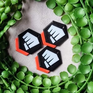 K&ouml;nnte beinhalten: Drei schwarze und wei&szlig;e Schl&uuml;sselanh&auml;nger in Faustform mit roten Umrissen. Die Schl&uuml;sselanh&auml;nger sind in Dreiecksform angeordnet.