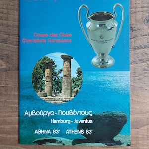 May include: A blue and white programme for the 1983 European Cup Final, featuring the European Cup trophy and a photo of the Acropolis in Athens, Greece. The text reads "European Cup Final, Hamburg vs. Juventus, Athens 83'"