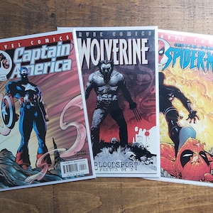 Puede incluir: Tres c&oacute;mics de Marvel con Capit&aacute;n Am&eacute;rica, Lobezno y Spiderman. El c&oacute;mic del Capit&aacute;n Am&eacute;rica muestra al h&eacute;roe con su escudo. El c&oacute;mic de Lobezno presenta al personaje con sus garras. El c&oacute;mic de Spiderman muestra al h&eacute;roe en acci&oacute;n.