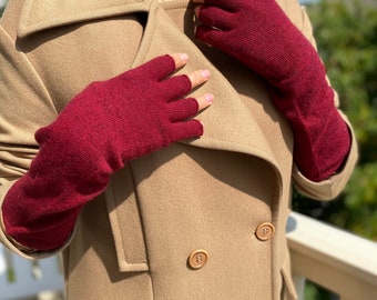 May include: A pair of burgundy fingerless gloves made of a soft, knitted fabric. The gloves are worn by a person wearing a camel-coloured coat.