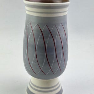 May include: A grey ceramic vase with a white base and red geometric design. The vase has a flared top and a wide base.