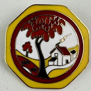 Może przedstawiać: Szpilka emaliowana w kolorze żółtym, czerwonym i białym z  stylizowanym obrazem domu, drzewa i płotu. Szpilka ma kształt ośmiokąta.