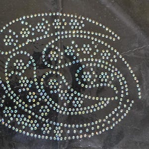 Può includere: Uno sfondo in tessuto nero con un grande disegno di un fiore stilizzato o un motivo floreale, scintillante e argentato.