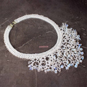 Könnte beinhalten: Eine weiße Perlenkette mit einem zarten, spitzengleichen Design und einem Fransenbesatz aus schillernden Opal-Steinen.