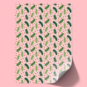 May include: A sheet of wrapping paper featuring a repeating pattern of cartoon pickles with smiling faces and small arms, interspersed with tiny red hearts on a light pink background. The paper has a curled corner showing a white underside.