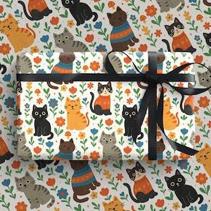 May include: Gift wrap featuring a repeating pattern of cartoon cats in various colors, including orange, black, and gray, interspersed with flowers and mushrooms on a white background. A black ribbon is tied around the wrapped gift.
