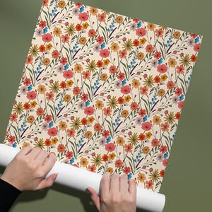 May include: A roll of wallpaper featuring a repeating pattern of wildflowers in shades of red, orange, yellow, and blue on a cream background. The design includes various small blossoms, thin green stems, and delicate leaves throughout.