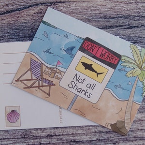 May include: A postcard with a beach scene featuring a palm tree, a beach chair, and a sign that reads "Don't Worry, Not all Sharks". The sign is yellow with a black shark silhouette. The postcard is watercolor style with a blue ocean and sandy beach.