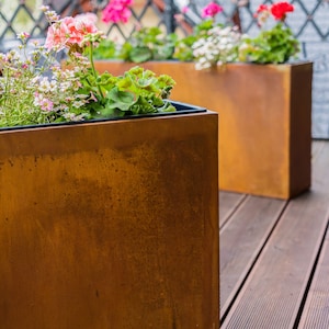 May include: Two rusty brown metal planters with pink, white and red flowers. The planters are on a wooden deck.