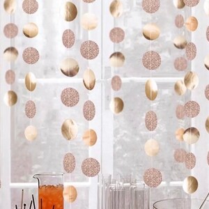 May include: A decorative garland consisting of multiple vertical strings featuring alternating rose gold circular discs. The discs include both smooth metallic finishes and textured glitter finishes, hanging in a repeating pattern to create a festive display.