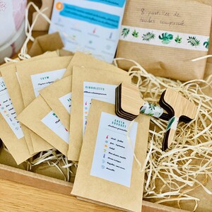 Puede incluir: Una caja de cart&oacute;n marr&oacute;n llena de virutas de papel marr&oacute;n. La caja contiene peque&ntilde;os paquetes de papel marr&oacute;n etiquetados con los nombres de hierbas, como "Tomillo" y "Cebollino". Tambi&eacute;n hay marcadores de plantas de madera y una peque&ntilde;a bolsa de papel marr&oacute;n etiquetada como "Aneth Bouquet". La bolsa enumera los meses del a&ntilde;o y las hierbas correspondientes para plantar.
