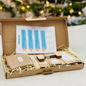 Puede incluir: Una caja de cart&oacute;n marr&oacute;n llena de suministros de jardiner&iacute;a. La caja contiene paquetes de semillas, marcadores de plantas de madera y una hoja de instrucciones de jardiner&iacute;a. La hoja de instrucciones tiene cuatro pasos con los n&uacute;meros del 1 al 4.