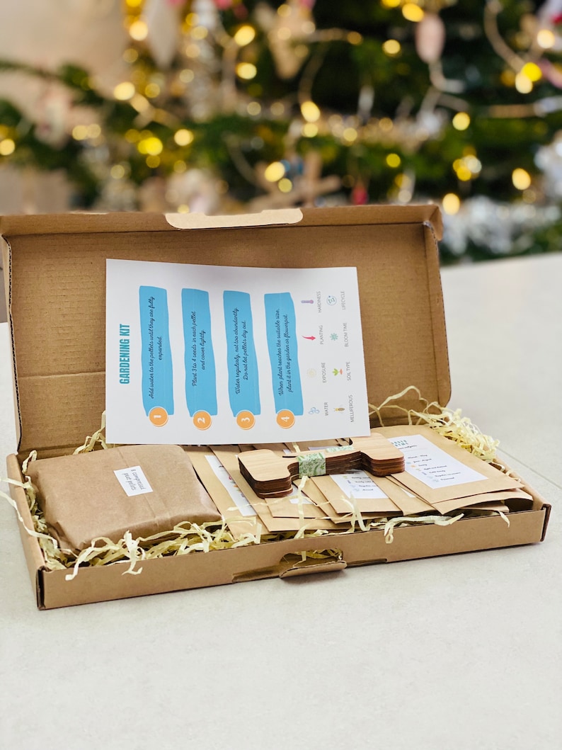 Puede incluir: Una caja de cart&oacute;n marr&oacute;n llena de suministros de jardiner&iacute;a. La caja contiene paquetes de semillas, marcadores de plantas de madera y una hoja de instrucciones de jardiner&iacute;a. La hoja de instrucciones tiene cuatro pasos con los n&uacute;meros del 1 al 4.
