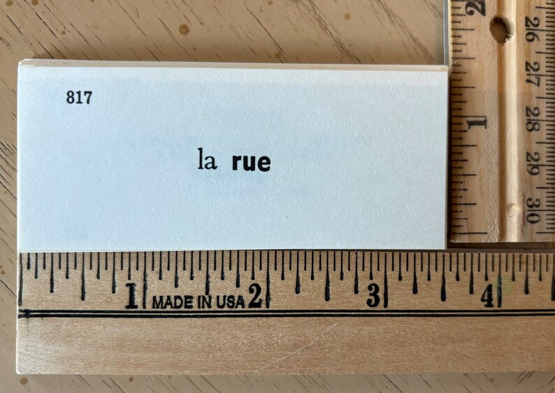 Op de afbeelding: Een witte indexkaart met het nummer 817 gedrukt in de linkerbovenhoek. De tekst "la rue" is in het zwart in het midden van de kaart gedrukt.